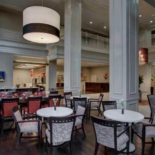 A modern restaurant interior with a dining area featuring several tables and chairs, a bar, and stylish lighting.