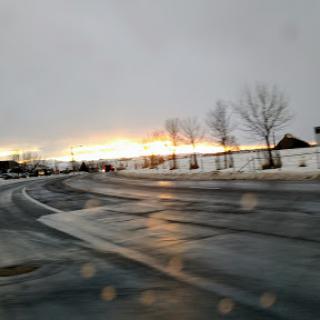 A serene winter sunset marks the end of the day, casting a warm glow over a snow-covered road.