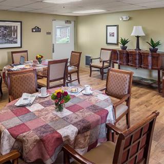 A cozy dining room with neatly arranged tables and chairs, featuring floral centerpieces and warm decor.