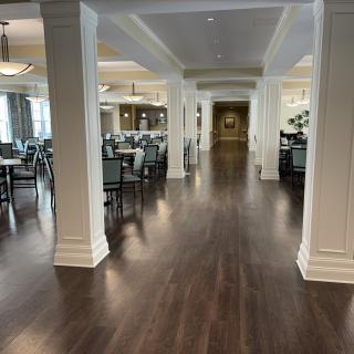 An elegant dining area with polished hardwood floors and neatly arranged tables, illuminated by soft overhead lighting.