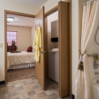 A view from a bathroom into a cozy bedroom, featuring a robe hanging on the door and a shower curtain to the side.