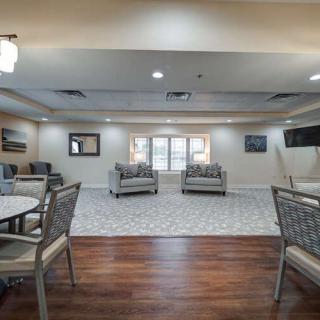 A comfortable lounge area with seating and tables, featuring a mix of carpet and hardwood flooring.