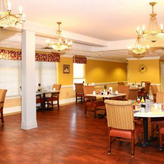 A well-lit dining room interior with several tables and chairs, featuring elegant lighting and wooden flooring.