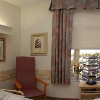 A hospital room featuring a chair, artwork on the walls, and a window with curtains.