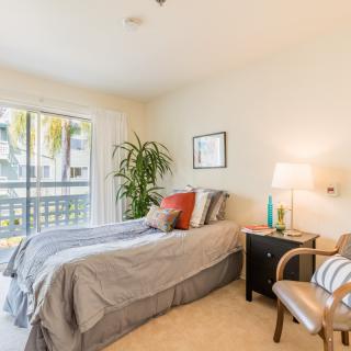 A cozy bedroom with a neatly made bed, nightstand, and chair by the window.
