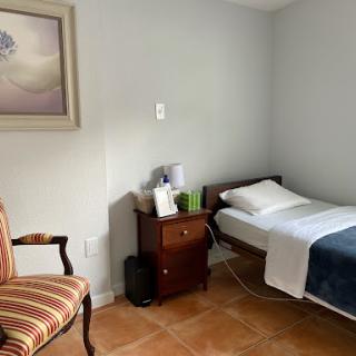 A simple and cozy room featuring a bed, a comfortable chair, and a decorative painting on the wall.