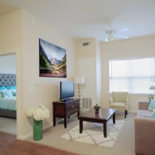 A bright and well-decorated living room with a view into a bedroom, featuring modern furniture and decor.