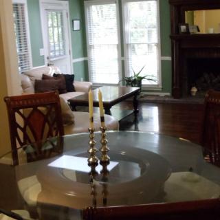 A cozy living room and dining area featuring a round glass table with decorative candle holders, wooden chairs, a sofa, coffee table, and a fireplace in the background.
