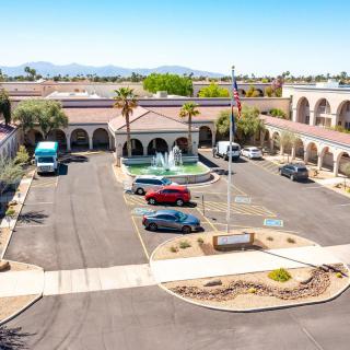 Aerial view of a building with arches, parking lot, and fountain surrounded by a desert landscape.