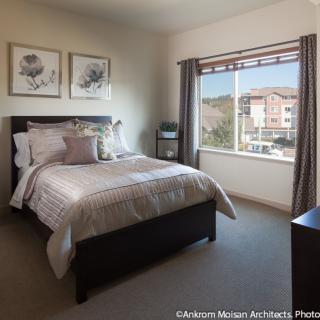 A cozy bedroom with a neatly made bed, large window, and decorative artwork on the wall.