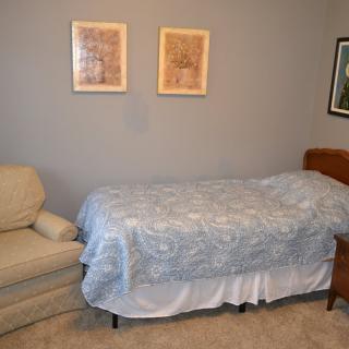 A simple bedroom with a bed, chair, and wall art.