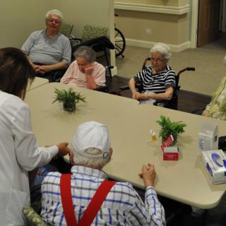 A group of elderly individuals gathered around a table with a caregiver in a nursing home setting.