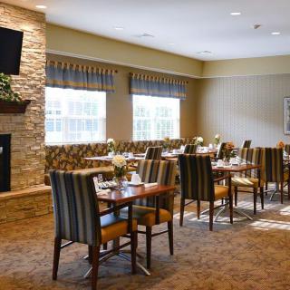 A cozy dining room with tables and chairs, featuring a fireplace and large windows.
