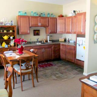 A cozy kitchen with wooden cabinets and a small dining area, featuring decorative elements and various kitchen appliances.