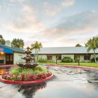 The exterior view of a hotel features a landscaped entrance with a central fountain.