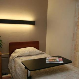 A simple hospital room with a bed, overbed table, and ambient lighting.