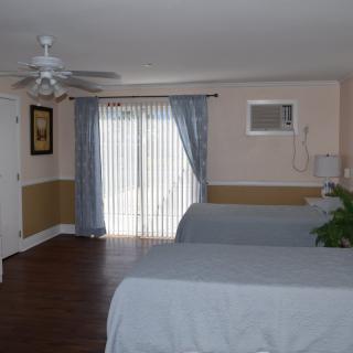 A spacious bedroom with two beds, ceiling fan, and large sliding glass doors with curtains.