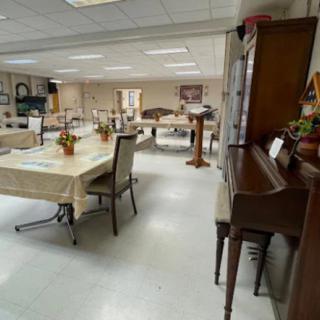 A community center room with dining tables and a piano, ready for an event.