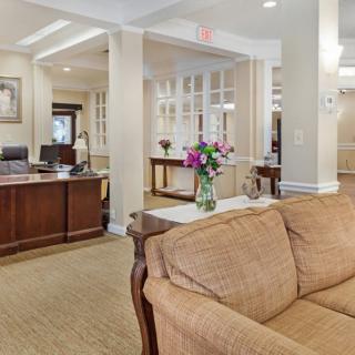 A cozy reception area featuring a brown sofa, a wooden desk, and floral decorations.
