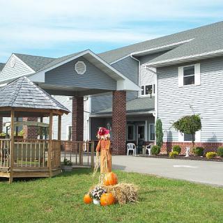 A building with a gazebo and autumn decorations on the lawn, including pumpkins.