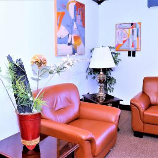 A cozy waiting room with leather chairs, colorful artwork, a lamp, and indoor plants.
