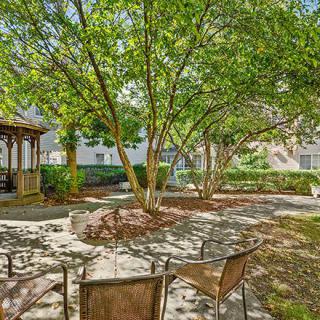 A peaceful garden setting with a gazebo and chairs under the shade of trees.