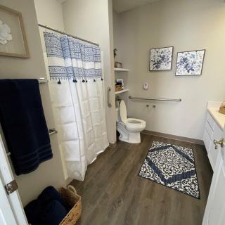 A modern bathroom with blue and white decor, featuring a shower, toilet, and open shelving.