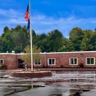 A brick building with a flagpole in the foreground, surrounded by trees under a blue sky.