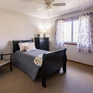 A cozy bedroom with a neatly made bed, a chair, and natural light coming through the window.