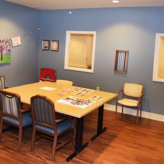 A cozy meeting room with a wooden conference table surrounded by chairs, decorated with artwork and featuring blue walls.