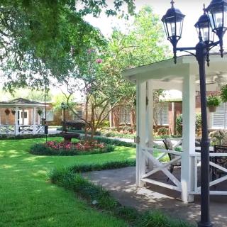 A tranquil garden featuring a gazebo, lush greenery, and manicured lawns.