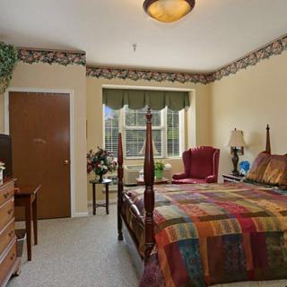 A cozy bedroom featuring a four-poster bed, plush armchair, and decorative window treatments.