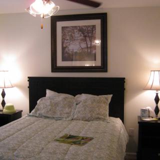A cozy bedroom featuring a neatly made bed, two elegant lamps on side tables, and framed artwork above the headboard.