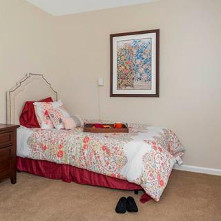 A cozy bedroom with a single bed adorned with a colorful bedspread, next to a wooden nightstand and framed artwork on the wall.