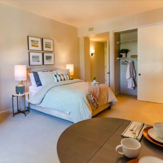 A cozy bedroom interior with a neatly made bed, soft lighting from bedside lamps, and an open closet.