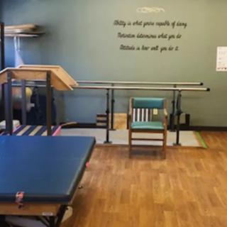 A physical therapy room equipped with parallel bars and a gym mat.