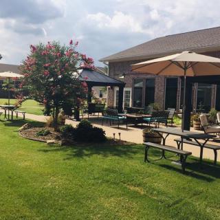 A peaceful garden patio with tables, chairs, and umbrellas surrounded by well-maintained landscaping.
