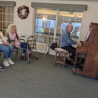 A pianist entertains an audience of elderly individuals in a cozy indoor setting.