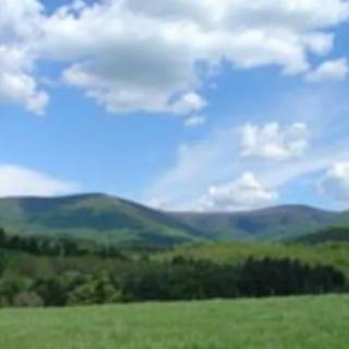 A scenic view of lush green hills and mountains under a blue sky with fluffy clouds.