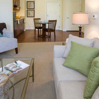 A cozy living room with a modern design, featuring a sofa, cushions, coffee table, and adjacent dining area.