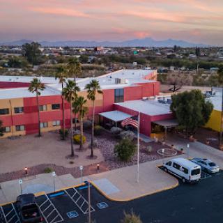 A serene aerial view of a modern building surrounded by palm trees during sunset.