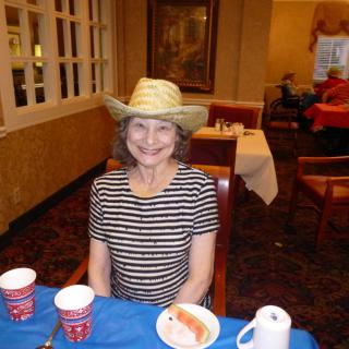 A woman wearing a hat and striped shirt is smiling while seated at a restaurant table.