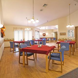 A cozy dining room with neatly arranged tables and chairs, adorned with decorative lighting and a wooden floor.