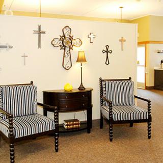 A cozy living area featuring striped chairs, a decorative lamp, and various crosses on the wall.