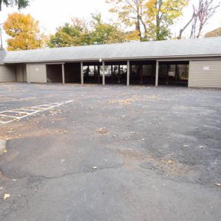 An empty outdoor pavilion with a paved parking area surrounded by trees in autumn.