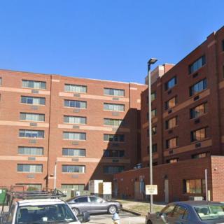 A brick apartment building with a parking lot in front under a clear blue sky.