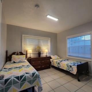 A cozy bedroom featuring two single beds with geometric patterned bedding, a dresser with lamps, and a large window allowing natural light to fill the space.