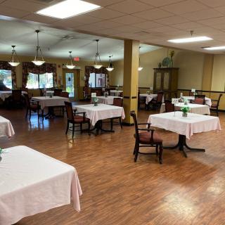 An empty dining room with tables covered in white linens, ready for service.