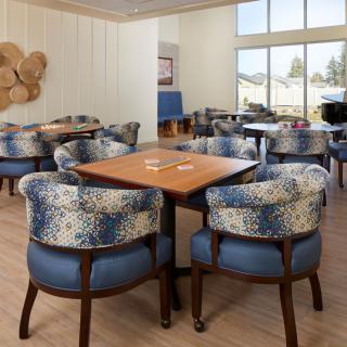 A modern lounge area featuring cozy chairs and tables, with ample natural light from large windows.