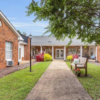A charming brick building with a central walkway, flanked by well-maintained gardens and a cozy bench.